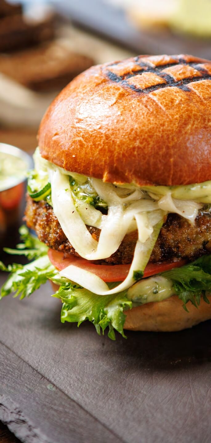 A close-up of a sandwich with lettuce, tomato, and cheese on a brioche bun.