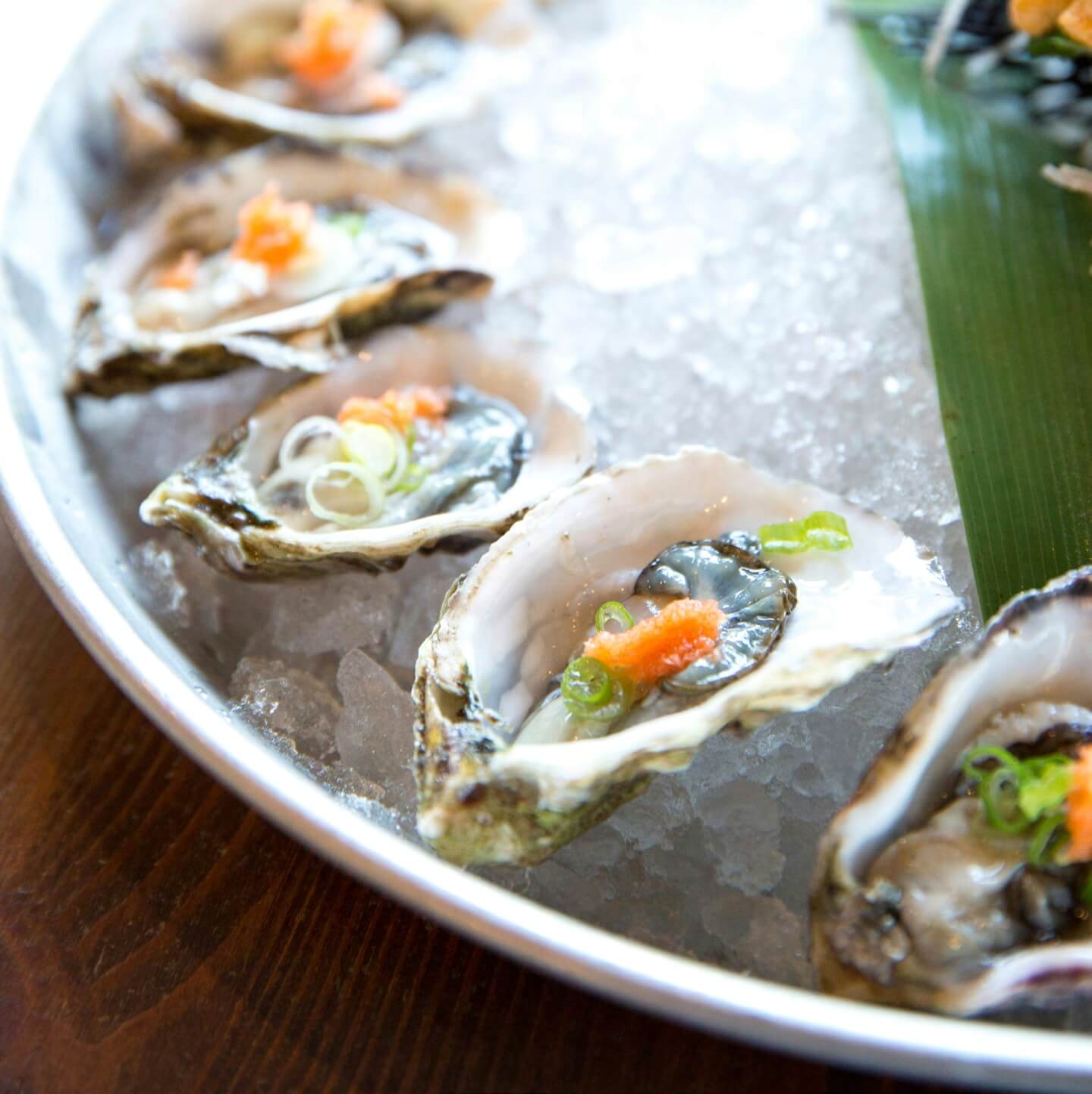 Fresh oysters on the half shell with garnishes, served on ice in a metal tray.