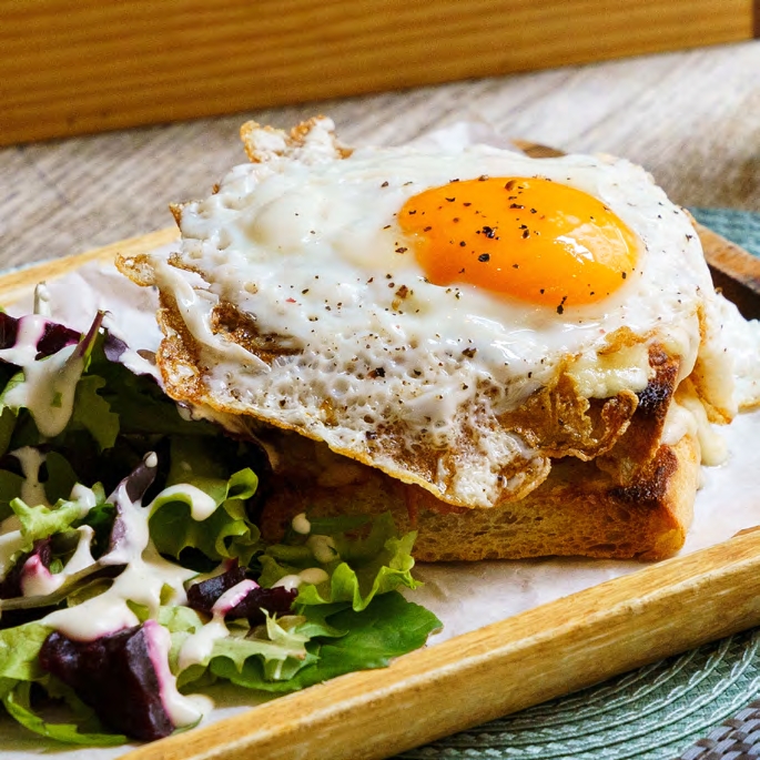 A fried egg on toast with a side of leafy green salad drizzled with creamy dressing.